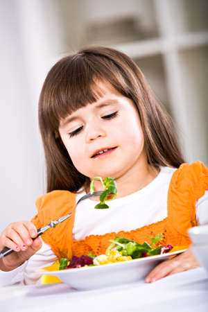 young girl eating salad at home. A studio shoot.の写真素材