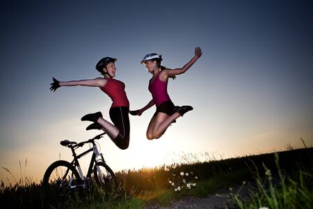 A cycling woman jumps and cheers in front of rural landscapeの写真素材