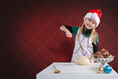 little girl making xmas cookies in front of red backgroundの写真素材