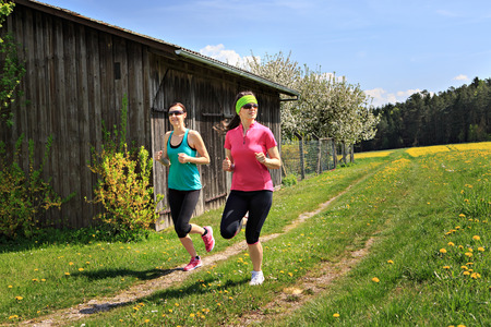 two women jogging through fields at the springtimeの写真素材