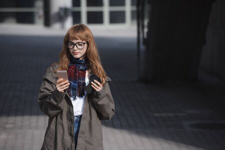 a bohemian style woman with red hair is using an application in her smartphone device in a modern architecture city environment while holding a cup of cofeeの写真素材