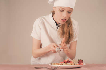 woman chef is spreading powdered sugar on a strawberry crepeの写真素材