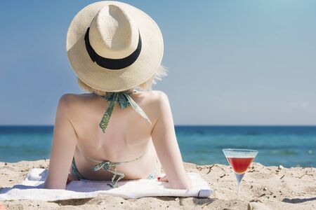 beautiful young woman lying on the beach next to a martini cocktailの写真素材