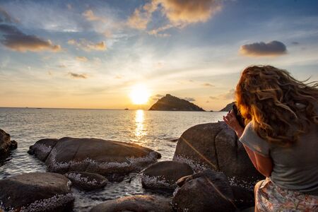 Women taking picture of island by sunsetの写真素材
