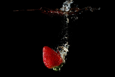 fresh healthy strawberry falling into water and injected and produced bubbles with black backgroundの写真素材