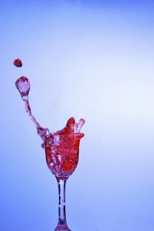 red liquid bubbling in a small glass with blue backgroundの写真素材