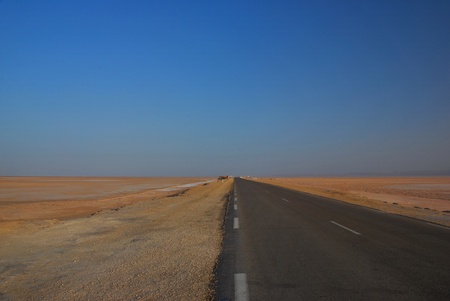 wide road in the desert with blue sky left and right only sand and saltの写真素材