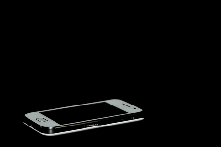 white mobile phone lying down on black backgroundの写真素材