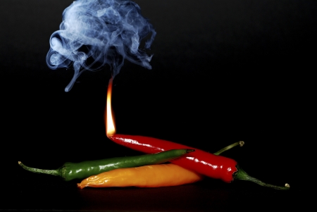 three different colored chilli pepper with flame and smoke on black backgroundの写真素材