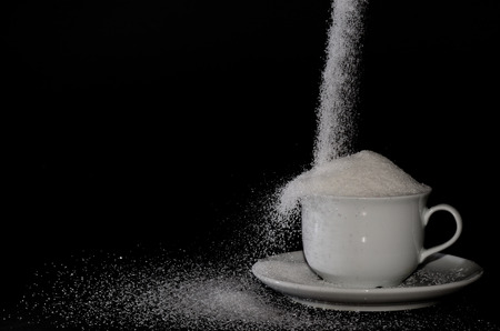 white cup full of sugar and black backgroundの写真素材