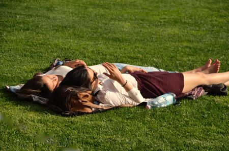two young women lying in the green grass in the sunの写真素材