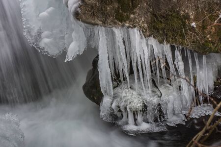 thin icicles on a rock near a waterfall in winterの写真素材