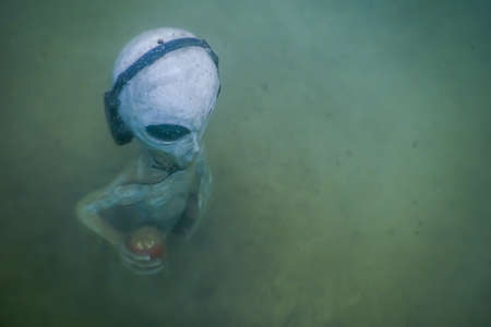 alien with headphones from above while diving in a lake in the mountains
