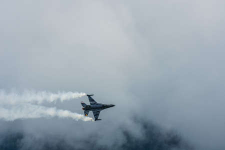fighter plane flies slowly at a air show with white dense rain clouds in the summer