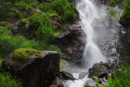 rushing large waterfall over rocks with green plants on the side while hiking