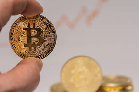 bitcoin held between two fingers with other coins in the background detail view