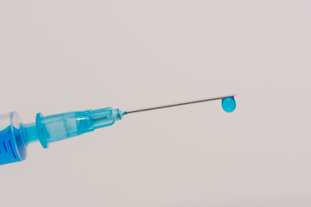 syringe with a blue fluid vaccine and a drop on the front view with white background