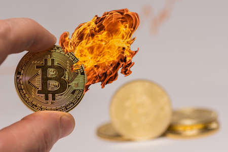 bitcoin held between two fingers with hot fire on the coin with other coins in the backgroundの写真素材