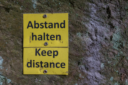 yellow sign on a rock with keep distance while hiking in the mountainsの写真素材