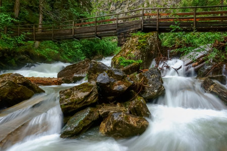wooden bridge over a wild mountain creek with huge rocks while hikingの写真素材