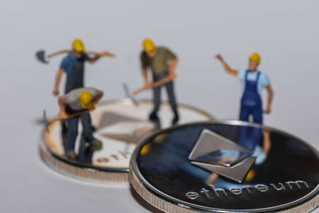 four miners standing in the background of a stack of silver ether crypto currency on gray backgroundの写真素材