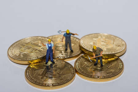three miners standing on five gold bitcoins crypto currency with gray backgroundの写真素材