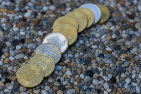 many valueable golden and silver coins bitcoin ether and ada from cryptocurrency lying on little stones in a rowの写真素材