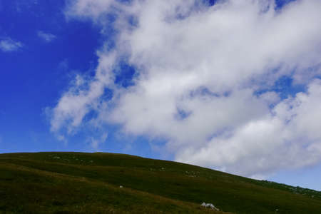 round hill with grass on a mountain with wonderful clouds on the blue sky