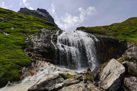 gorgeous waterfall over high rocks while hiking to the top of a mountain in the summerの写真素材