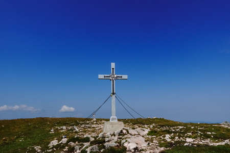 silver summit cross on a green mountain with rocks and deep blue sky in the summerの写真素材