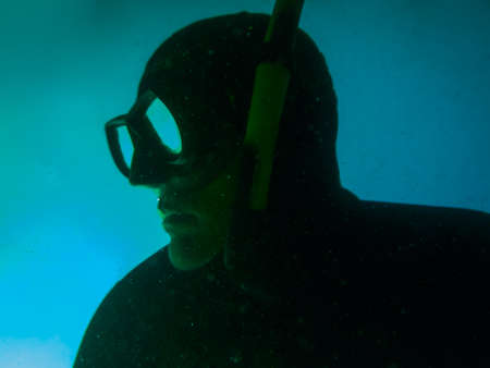 man while freediving in dive suit and mask in the deep with cold blue water