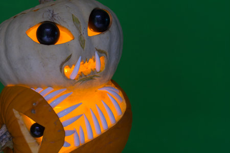 dinosaur pumpkin bites into an alien pumpkin with green background detail left at halloweenの写真素材