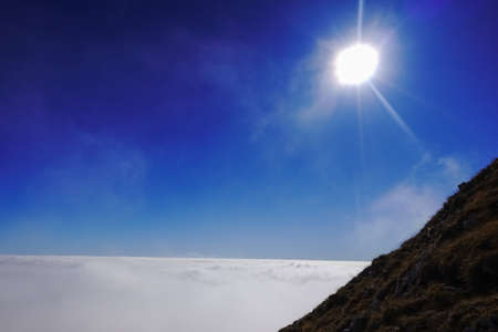 very dense fog under shining sun on blue sky while standing on a mountainの写真素材