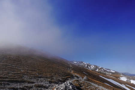 hiking path with hiker on a oblique mountain with half fog and blue sky in austriaの写真素材