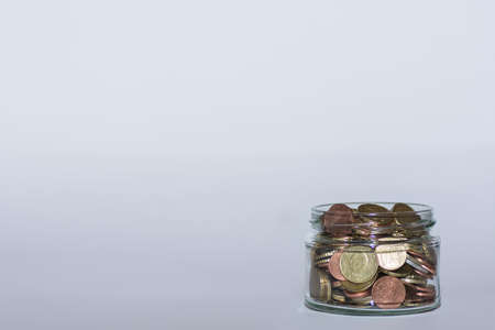 saved money in a flat glass with many different euro coins for financial independence with gray backgroundの写真素材