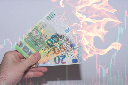 hand helding three burning and disolving euro bank notes with a chart from the finance market