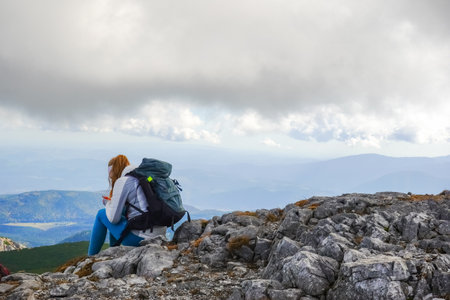 single female hiker sits on rocks on the top from a mountain in austriaの写真素材