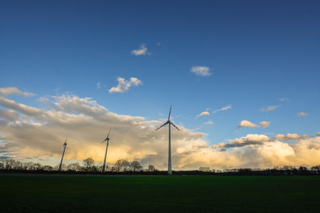 dense colorful rainclouds with blue sky and a flat landscape with three windmillsの写真素材