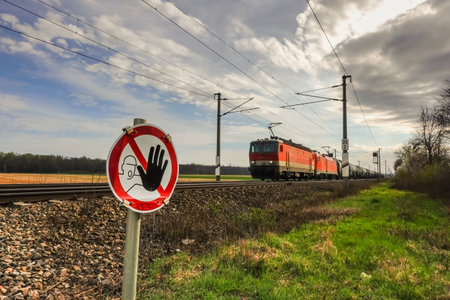caution sign at a crossing with an approaching fast train with clouds at the skyの写真素材