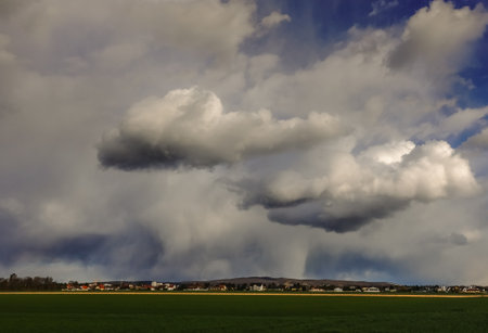 dense rain clouds over a village and fresh green fields in the foregroundの写真素材