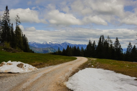 curvy dirt road for hiking in a mountain landscape with snow in austriaの写真素材