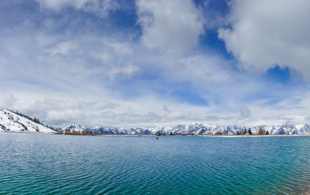 little waves in a wonderful mountain lake with a snowy mountain range and cloudy sky panorama viewの写真素材