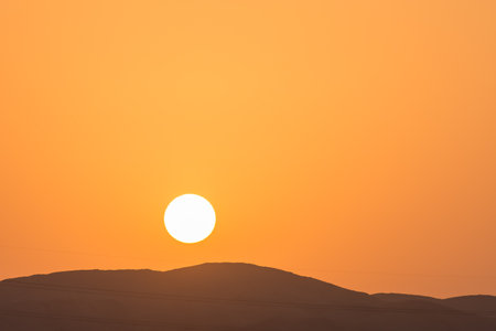 warm bright sun with orange sky over a black mountain on vacationの写真素材