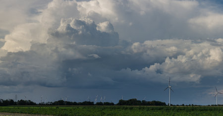 dark dense rainclouds over pinwheels on a green field panorama viewの写真素材