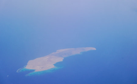 single island with coral reef in deep blue sea view during a flight on vacationの写真素材
