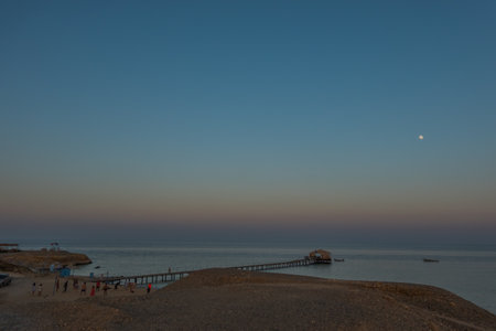Sunset over the sea with a pier in the foreground and the moon in the backgroundの写真素材