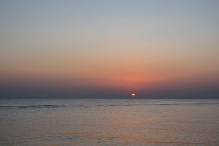 warm red sun at the horizon at the sea shortly after sunrise in egyptの写真素材