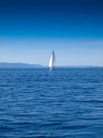 Front view of a sailing boat in an open blue sea and a clear blue skyの写真素材