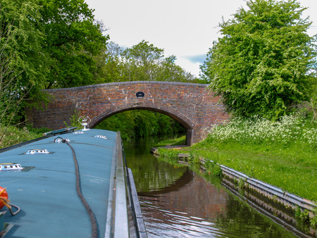 A narrowboat approaches a bridge on the Staffordshire and Worcestershire Canal in Staffordshire, England. View from the helmsman on the boat.の写真素材