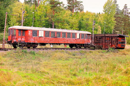 A picture of two rusty, old, abandoned train cars in a lush green landscape, one being toppled over on the track の写真素材